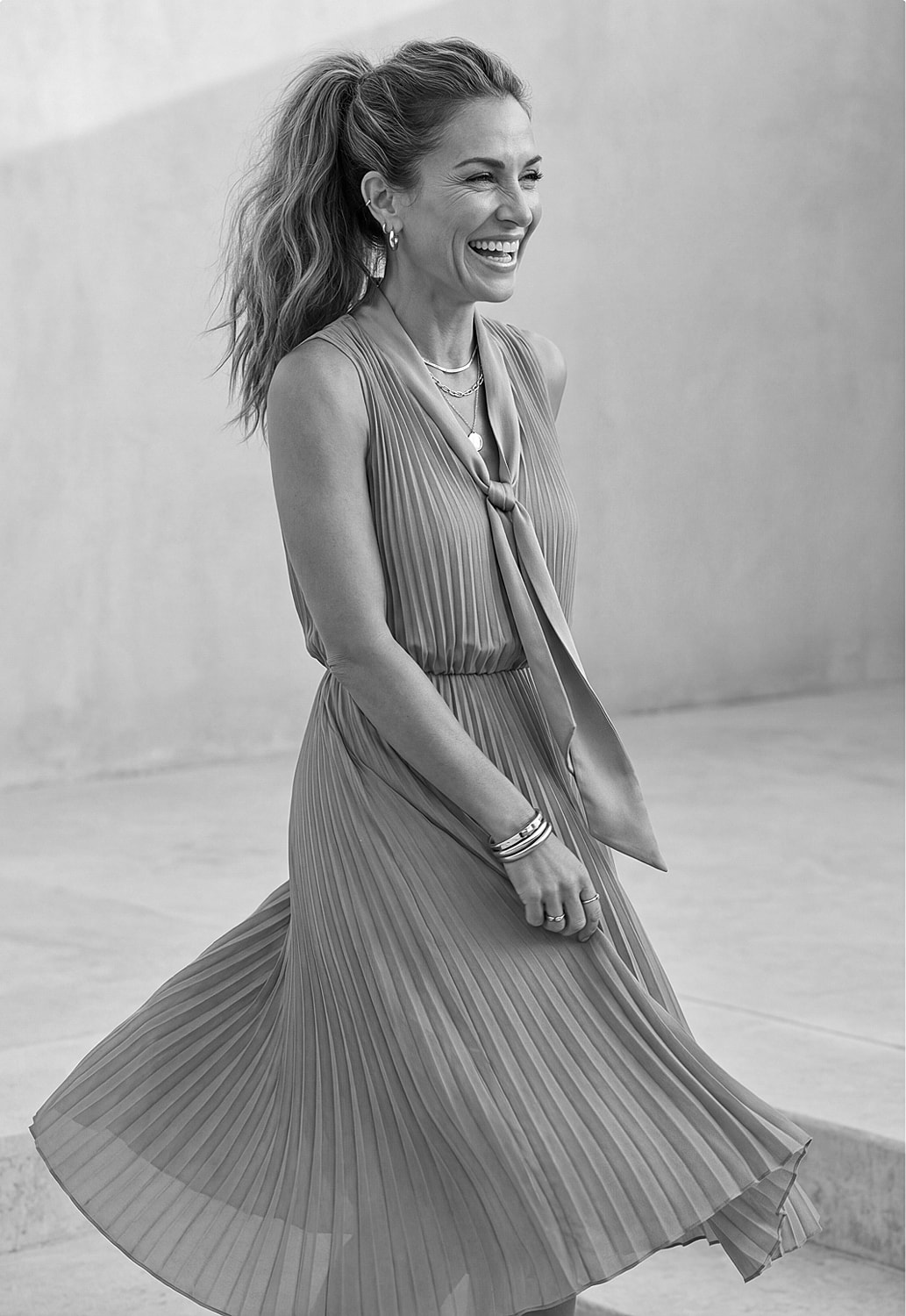 Woman in pleated dress smiling joyfully.